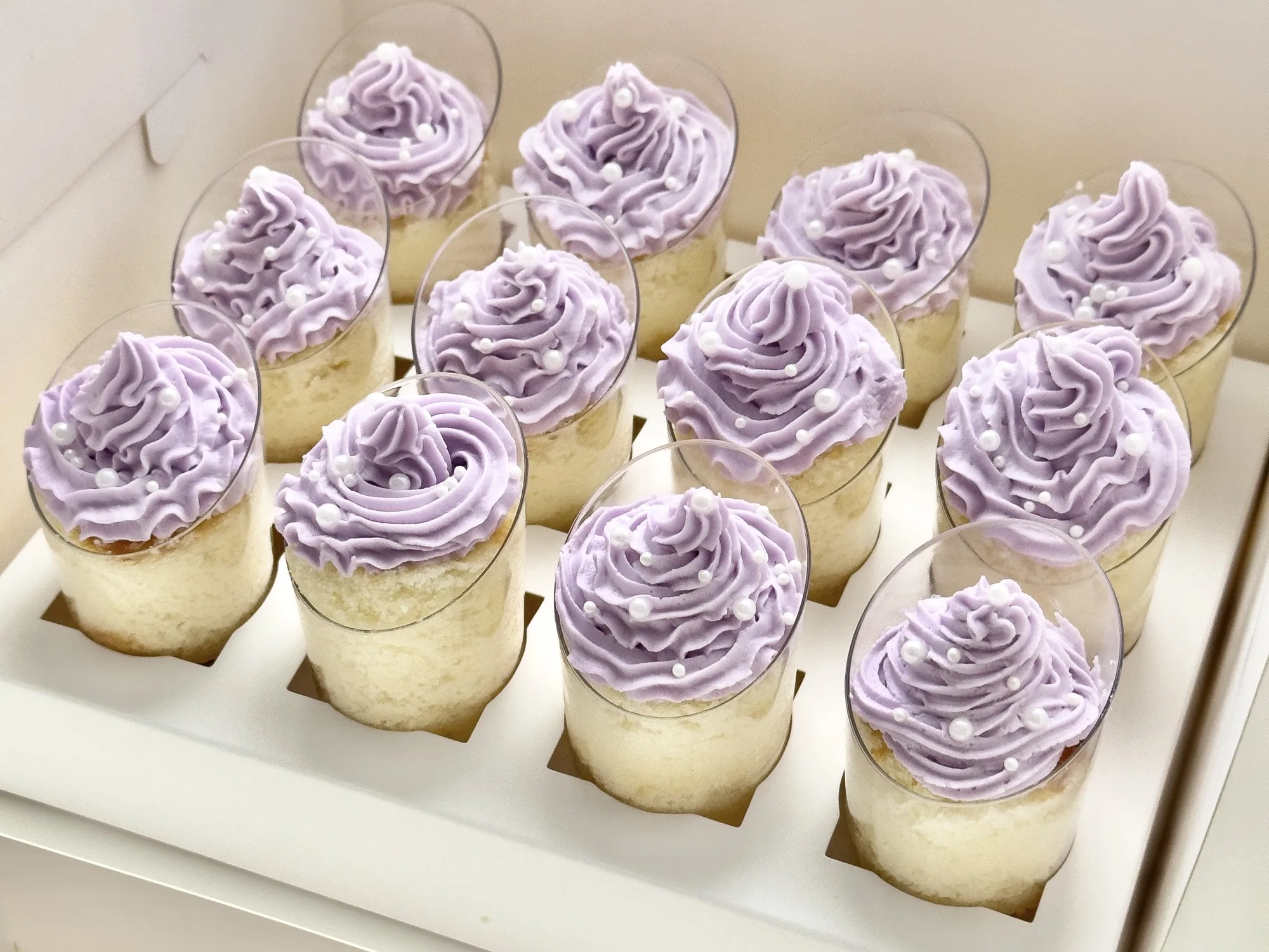 A white box of individual cake shooters piped with lavender buttercream swirls.