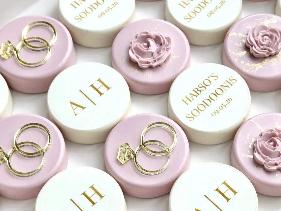 Pink and ivory chocolate covered Oreos printed with a gold monogram and event date.