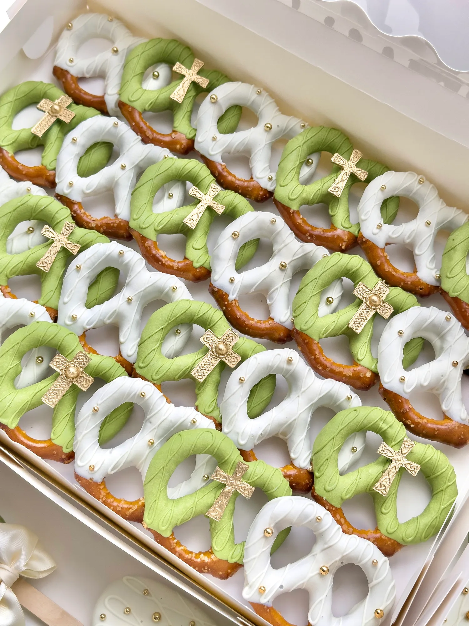 Light green and white dipped pretzels finished with small gold crosses, packed in a white box.
