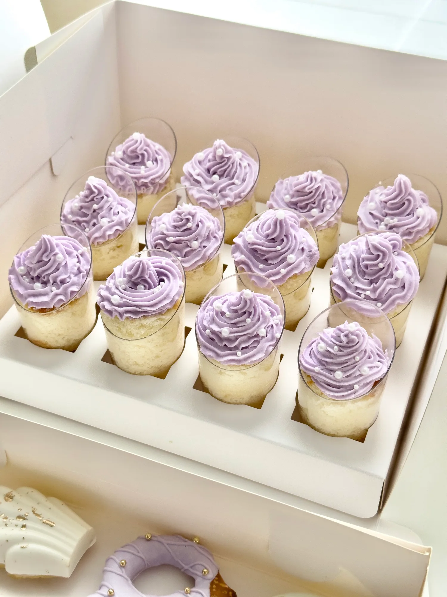 A white box of cake shooters piped with lavender buttercream swirls.