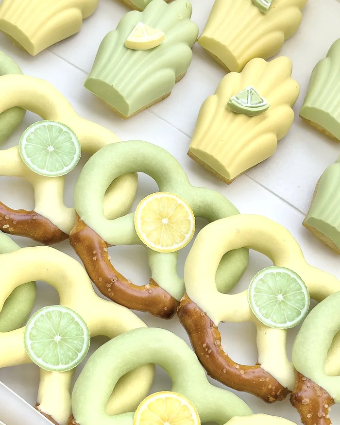 A box of chocolate dipped pretzels in pale green and yellow, each topped with a sugar lemon or lime slice.