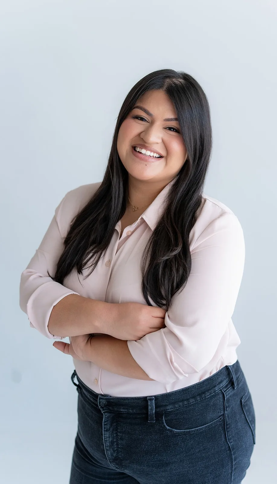 Maria, the owner of The Sweet Mission, laughs with her arms crossed in a blush blouse and dark jeans.