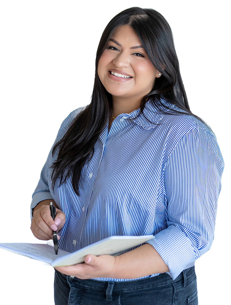 Maria, the owner of The Sweet Mission, standing in a blue striped shirt with a pen and an open notebook, smiling.