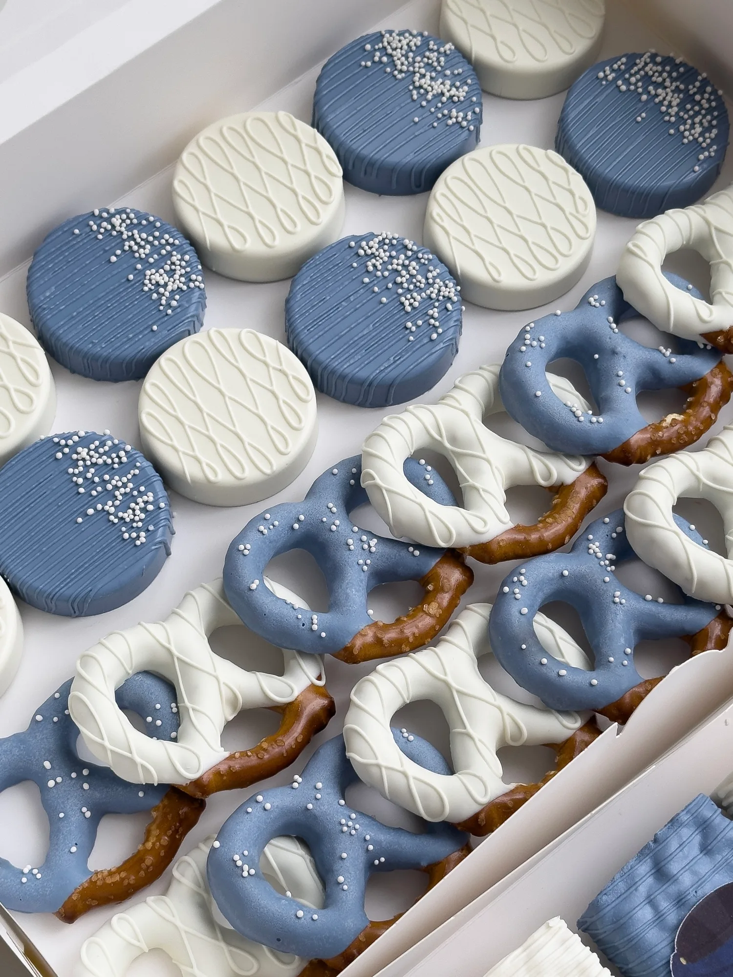 Navy blue and white covered Oreos dotted with white sugar pearls, beside navy and white dipped pretzels.