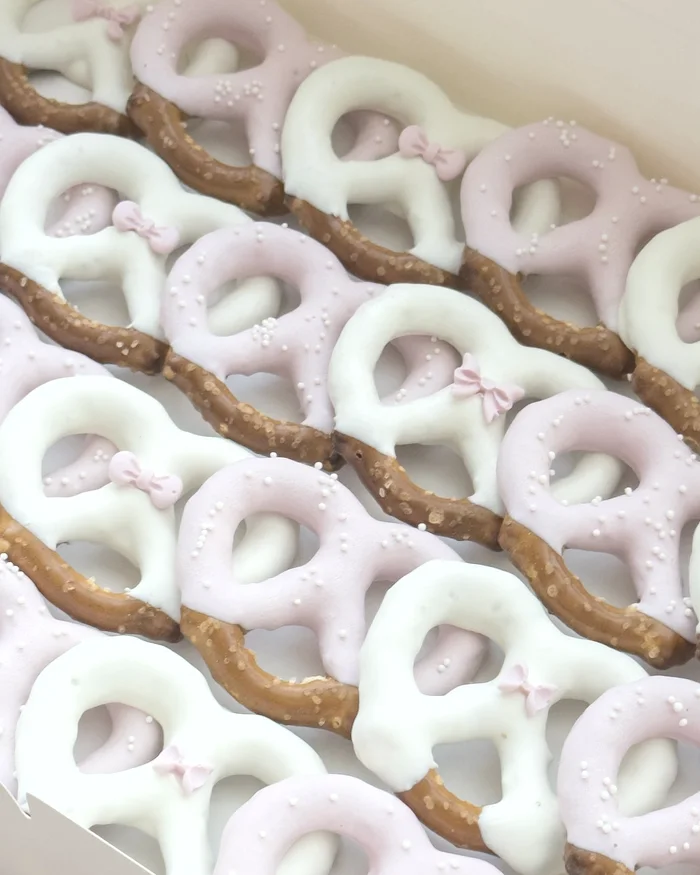 A box of pink and white chocolate dipped pretzels dotted with nonpareils and small sugar bows.