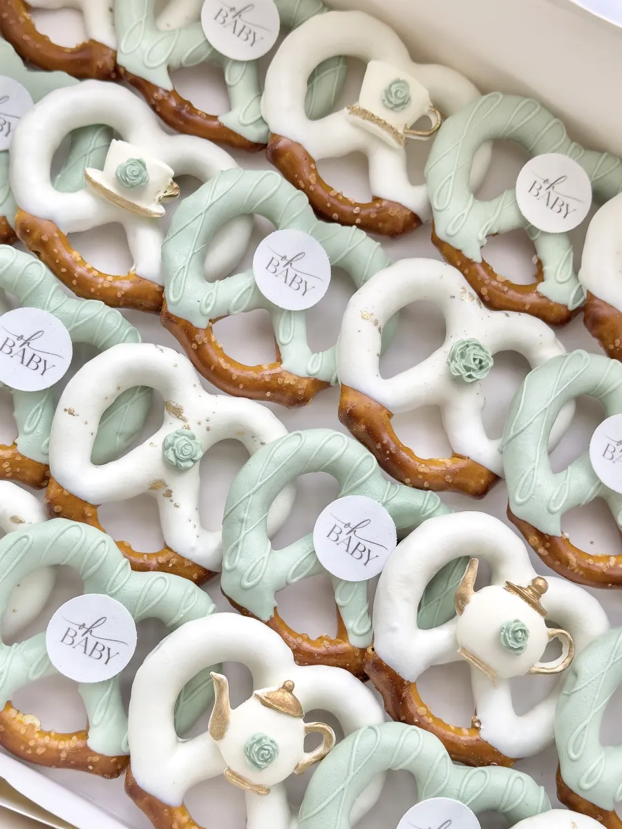 Sage green and white chocolate covered pretzels with mini sugar teapots, sugar roses, and round oh baby edible tags.