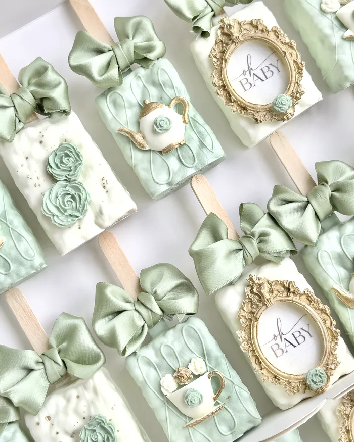 Sage green and ivory dessert bars with gold framed oh baby plaques, piped roses, sugar teapots, and satin bows.