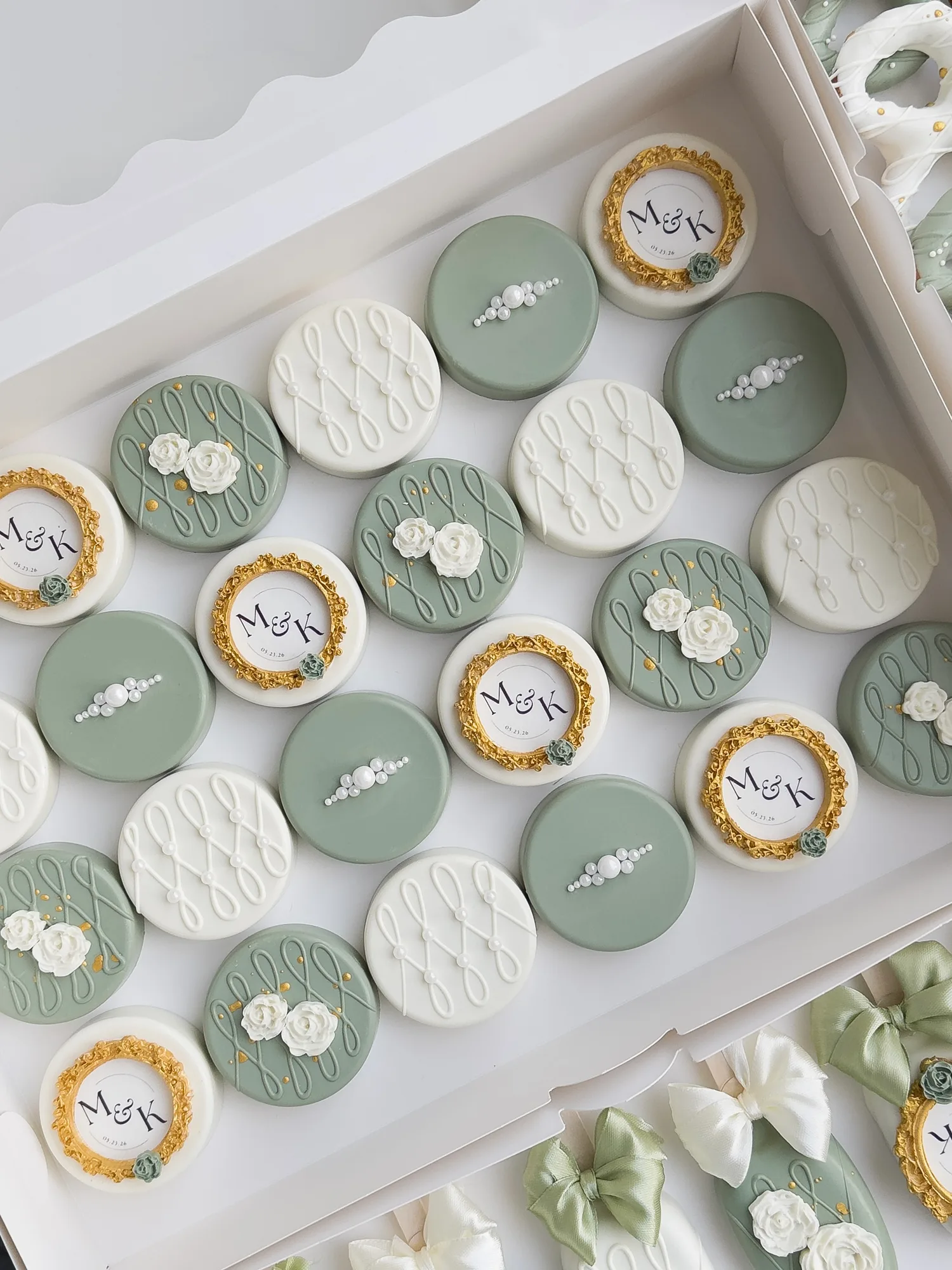 Sage green and ivory covered Oreos with gold framed monogram plaques, piped lattice, and small white sugar roses.