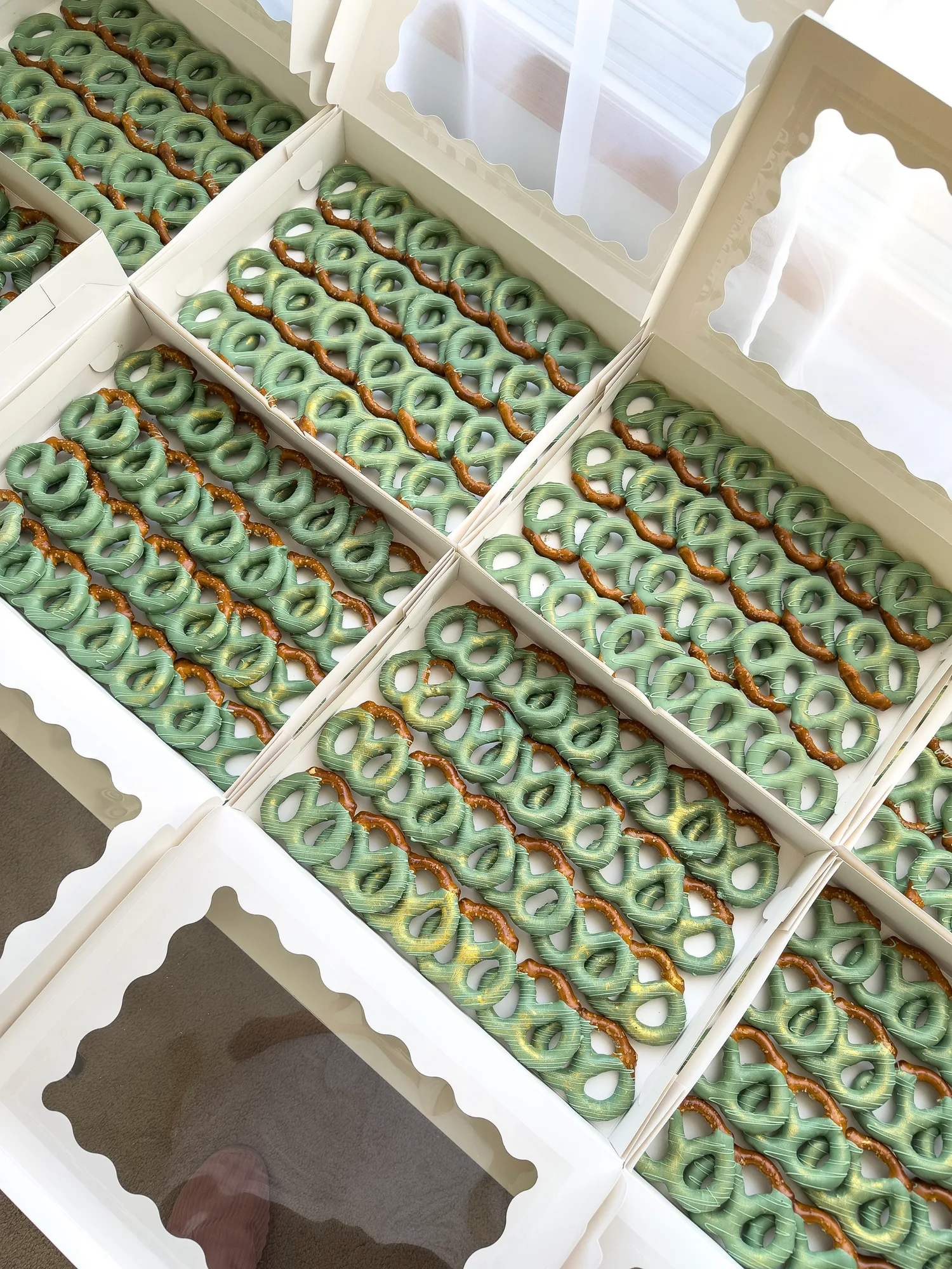Several open white boxes filled with rows of sage green chocolate dipped pretzels, packed for a large event.
