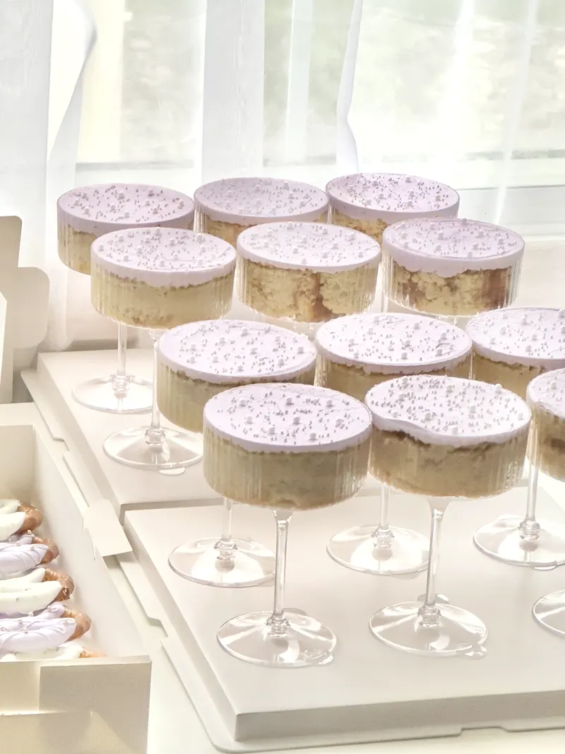 Lavender topped cake martinis in stemmed glasses, dusted with white sugar pearls, set out on a white display tray.